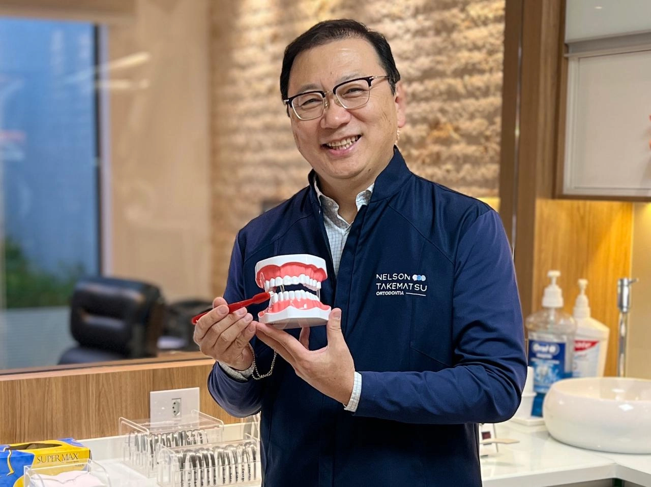 Dr. Nelson Takematsu demonstrando higiene e prevenção com modelo dentário no consultório em Mogi das Cruzes